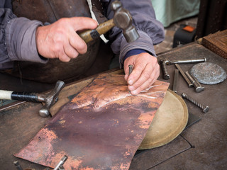 Detail of a craftsman engraves a copper plate with a hammer and chisel.