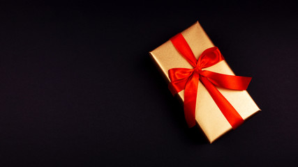 Golden gift with a red ribbon on a black background. Rozhdenvensky and New Year's concept. discounts and black friday