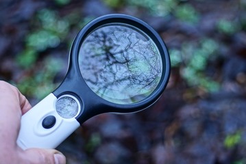 hand holds a big black white plastic magnifier outdoors