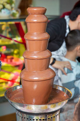 Chocolate fountain with fruits. Children birthday party . Homemade chocolate fountain fondue with marshmallow on a skewer dripping in chocolate sauce on blurred background and copy space .