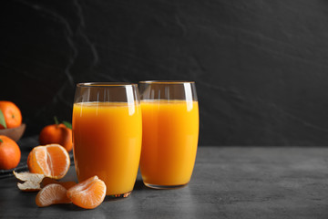 Fresh tangerines and glasses of juice on grey table