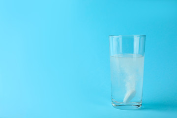 Glass of water with effervescent tablet on light blue background, space for text