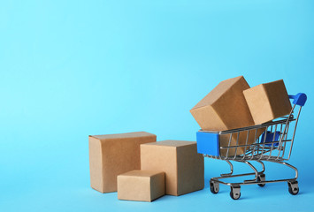 Shopping cart and boxes on light blue background, space for text. Logistics and wholesale concept © New Africa