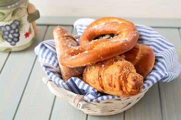 Many mixed breads and rolls on white basket and blue wooden background