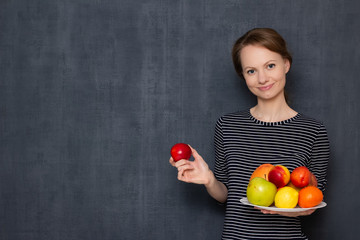 Portrait of happy young woman smiling and holding plate of fruits