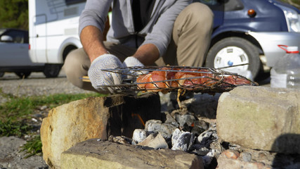 a man cooks meat on the grill outdoors on a background of motorhomes
