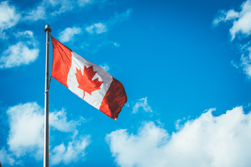 The Canadian flag in a blue sky with clouds