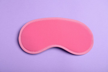Pink sleeping mask on violet background, top view. Bedtime accessory