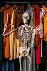 Artificial human skeleton model among clothes in wardrobe