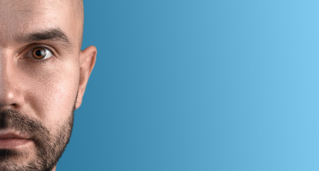 Fototapeta premium Half face portrait of a man with copyspace. Blue background