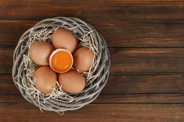 Raw chicken eggs in wicker nest on wooden table, top view