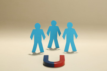 Magnet attracting paper people on beige background