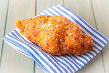 Tasty croissant with spikelets on blue and white napkin and wooden background