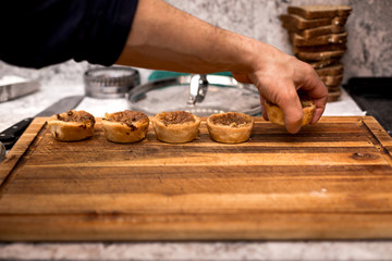 A row of butter tart cookies being laid on a wooden board by a pastry chef.