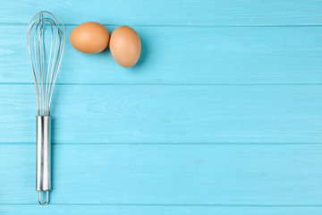 Raw eggs and whisk on light blue wooden table, top view with space for text. Baking pie