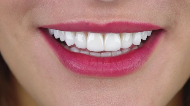 Beautiful woman with white dental veneers smiles amazingly and bites big juicy strawberry slice slow motion closeup