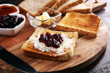 Toast bread with homemade strawberry jam and apricot marmalade on rustic table served with butter for breakfast or brunch on table