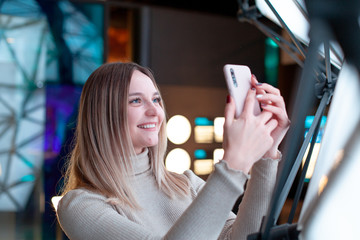 Young beautiful caucasian girl with blond hair and blue eyes smiling with smarphone between hands