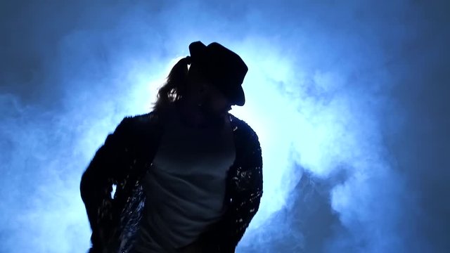 Silhouette of a young man dancer dancing in style Michael Jackson on a blue background of smoke. Close up, slow motion.