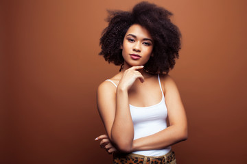 pretty young african american woman with curly hair posing cheerful gesturing on brown background,...