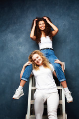 young pretty teenage girls friends with blond and brunette curly hair posing cheerful on blue background, lifestyle people concept