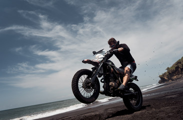 Naklejka premium Mężczyzna jedzie na motocyklu na plaży z czarnym piaskiem oceanu