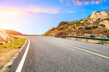 Asphalt highway and mountains with beautiful colorful clouds at sunset.