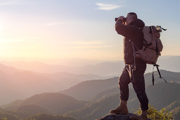 Young man with backpack enjoying sunset on binoculars peak of mountain layers line.Travel hiking.