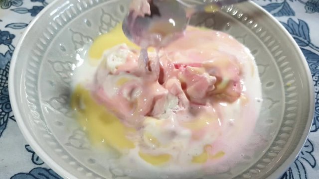 Strawberry, vanilla and black current flavored ice cream with yellow vanilla custard topping, delicious sunday dessert being scooped with stainless steel spoon in porcelain bowl.