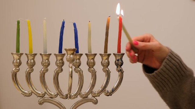 A woman's hand lighting candles in the menorah for Hanukkah