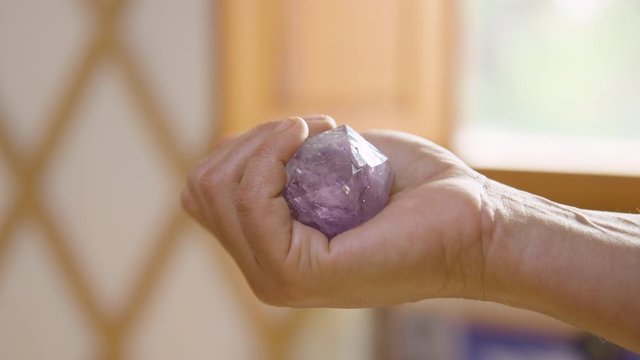 Close up of hand closing around a purple amethyst crystal in a yurt. 60fps