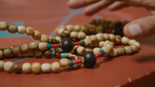A prayer Mala bead necklace is picked up from a table. 60fps