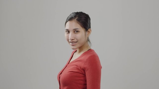 Young Asian woman with cute smile, no makeup and brunette hair pulled back poses and smiles in commercial advertising casting audition wearing red shirt