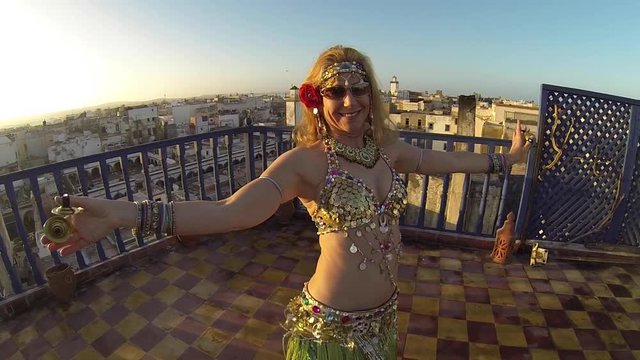 Camera pushes in on beautiful belly dancer as dances on the roof of a building in Morocco at sunset.