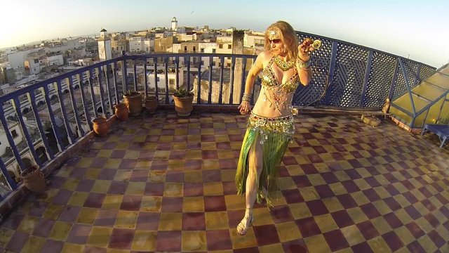 Smiling and happy belly dancer on the roof of a building in Morocco at sunset doing an Egyptian move.