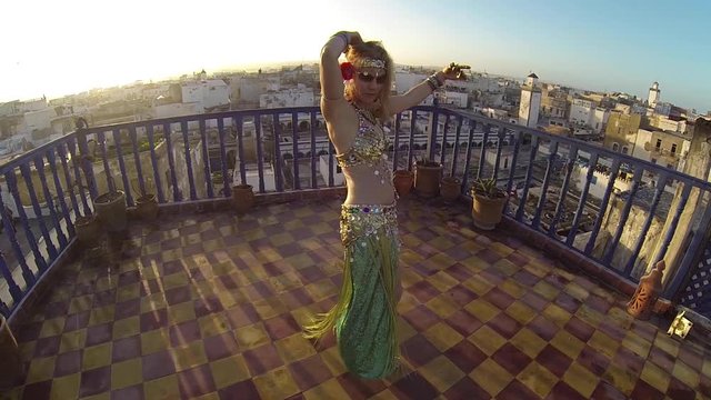 High angle closeup of belly dancer as she does the maya move on the roof of a building at sunset in Morocco.