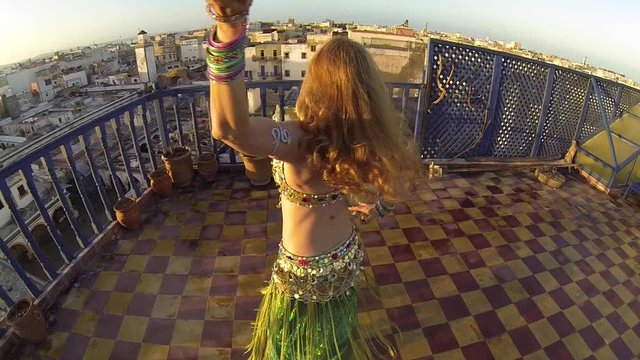 Beautiful dancer turning as camera turns opposite direction with setting sun on roof top in Essaouira, Morocco.