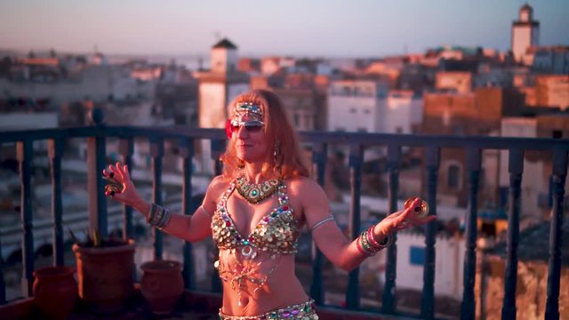 Beautiful belly dancer doing chest shimmies at sunset performing on a rooftop in Morocco.