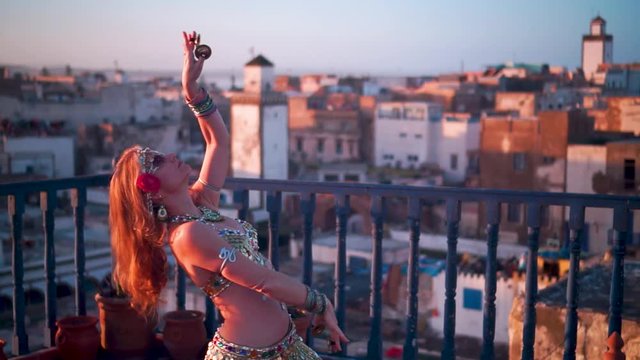 Beautiful belly dancer doing a back bend at sunset performing on a rooftop in Morocco.