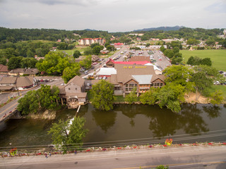 A local river runs through the tourist town of Pigeon Forge Tennessee with a water damn next to an active water wheel on a local building. A drone, birds eye, aerial view