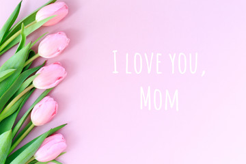 I love you, Mom wording with pink tulips on the pink background. Flat lay, top view. Mother's day holiday celebration card. Horizontal,