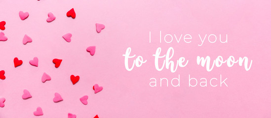 Love you to the moon and back wording and two tone heart sprinkles on the solid pink background. Romance, love, Valentines and mother's day concept. Flat lay, horizontal wide screen banner format
