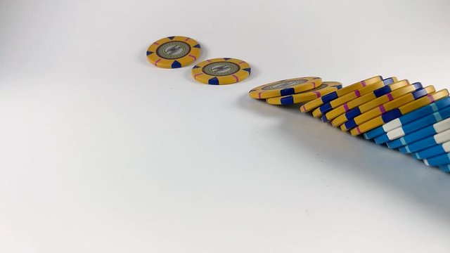 Stack of yellow and blue poker chips falling down on a white table, SLOMO, ISOLATED
