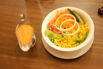 Fresh mixed salad with corn, carrots, lettuce, onions, and tomatoes, served with a creamy dressing on a wooden table. Perfect for healthy eating and restaurant menus.