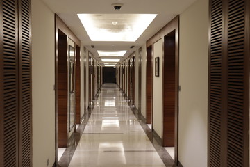Horizontal view of the brightly illuminated long tunnel shaped corridor with mirrors, wooden doors and cabinets on side walls