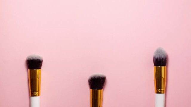 Stop motion animation top view of cosmetics brushes set for makeup at the bottom on pink background. Cosmetics and beauty concept. Make up concept with space for text