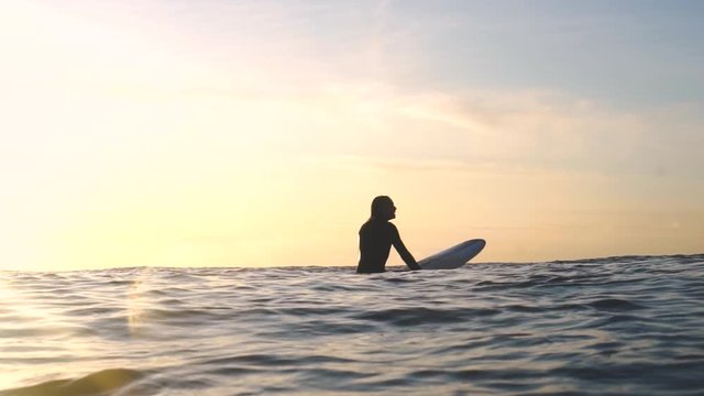 Longboarder woman waits on her board for the best wave, bathed in yellow golden light