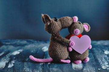 Handcrafted amigurumi rat hugs another knitted toy rat that holds the pink heart as a present....