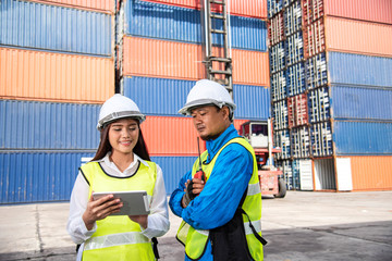 Logistics engineer and foreman checking their container loading list in tablet in container shipyard area with logistics area background, import export logistics business concept