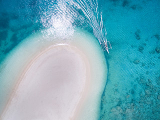 A small native bamboo and diesel boat outboard motors past a white sandbar beach in some crystal clear waters in the pacific islands in calm turquoise blue seas